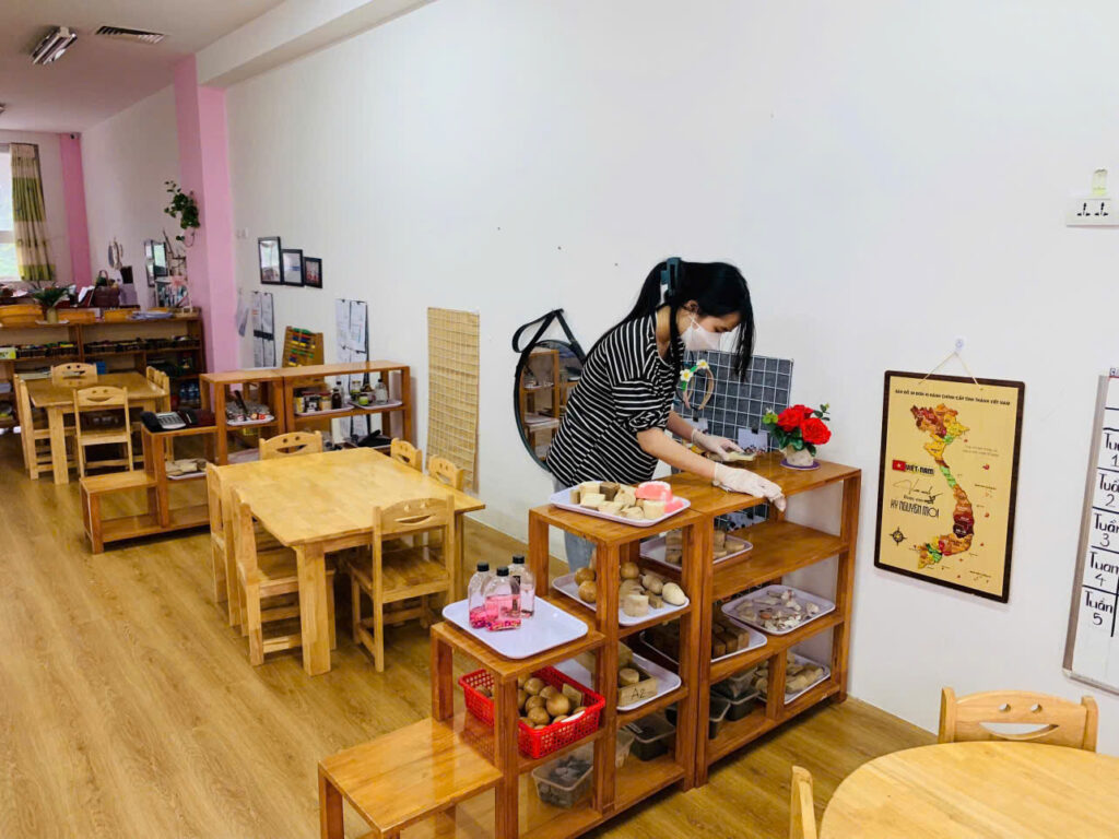 Cô giáo rửa và sấy khô đồ chơi tại trường mầm non, giảm nguy cơ lây nhiễm cúm A ở trẻ nhỏ.